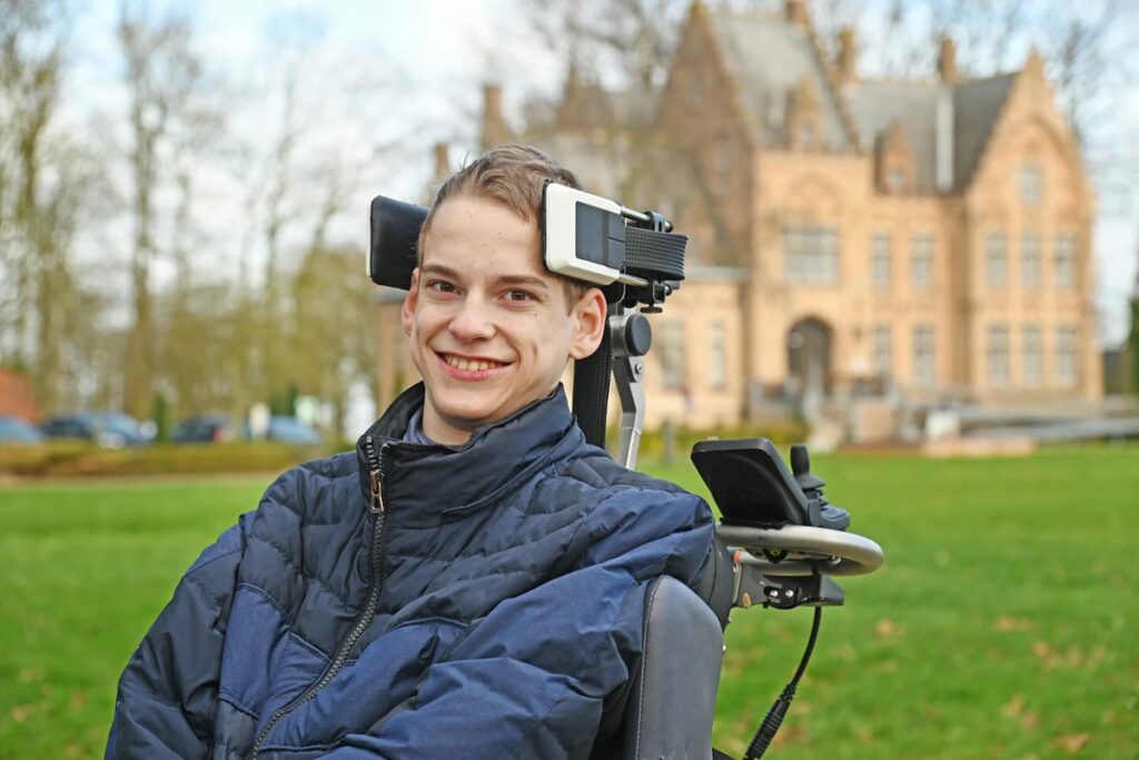 Young man in a powered wheelchair with CoMoveIT head control mounted on the headrest